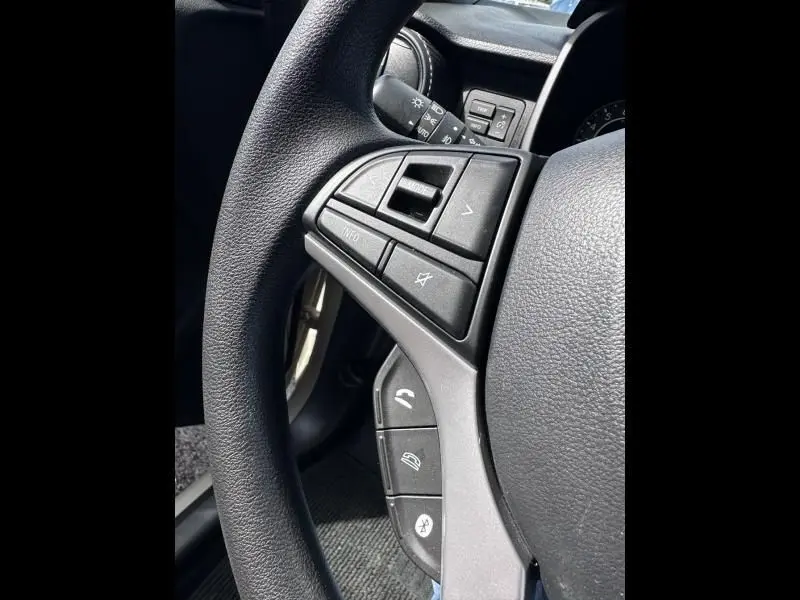 Gros plan sur les commandes au volant côté gauche du Suzuki Ignis beige 2023, avec boutons multifonctions et Bluetooth.