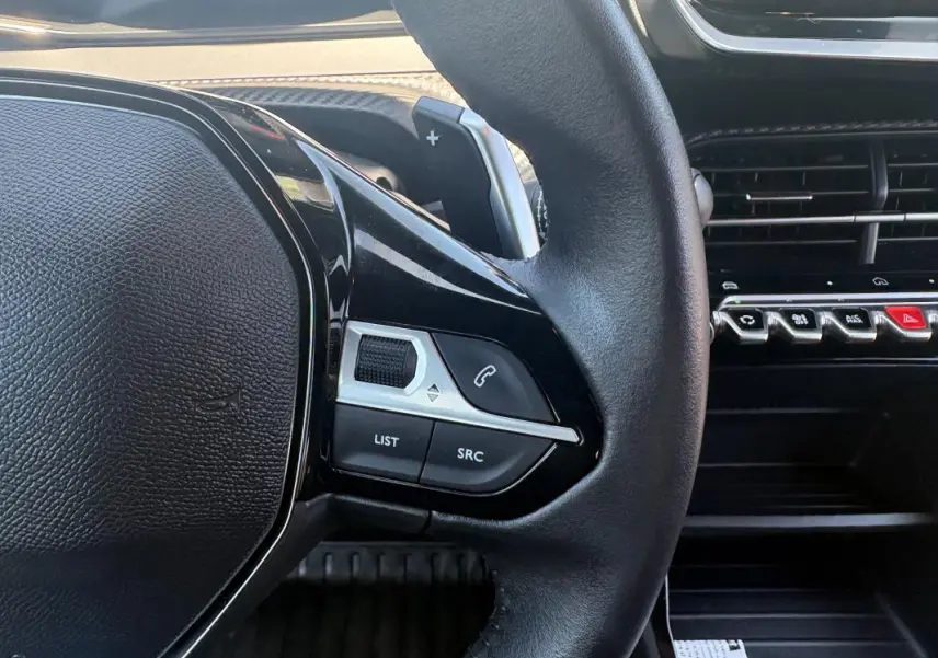Gros plan sur le volant côté gauche du Peugeot 2008 gris, avec commandes audio et tableau de bord noir.