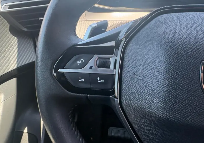 Gros plan sur le volant noir du Peugeot 2008 Hybrid 145 e-DCS6 Style, avec commandes audio intégrées côté gauche.