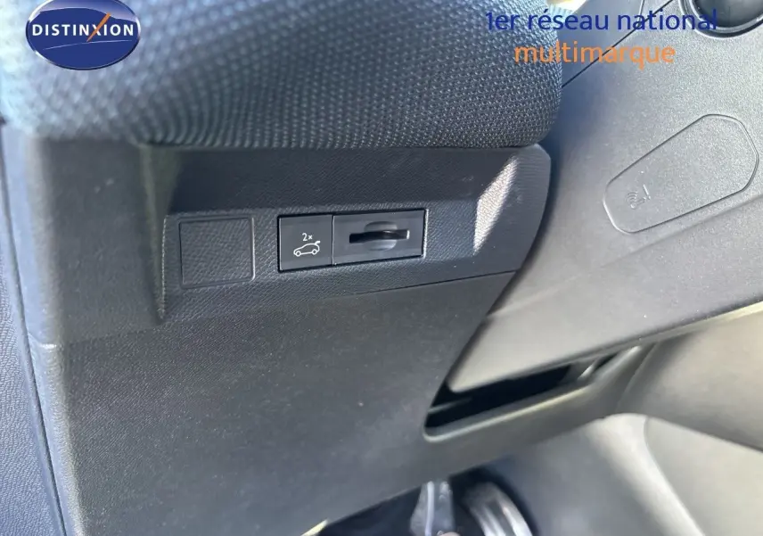 Détail intérieur montrant le bouton d'ouverture du coffre sur la partie inférieure gauche du tableau de bord noir.