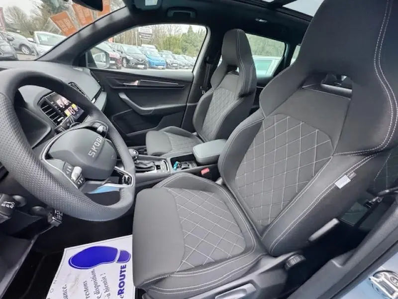 Vue intérieure côté conducteur du Skoda Karoq gris Diamant, sièges sport noirs avec surpiqûres, toit panoramique ouvert.