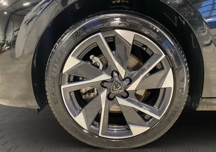 Gros plan sur la roue avant gauche noire perla nera d'une Peugeot 308 1.5 BlueHDi 130 Allure 2024 avec jante alliage distinctive.