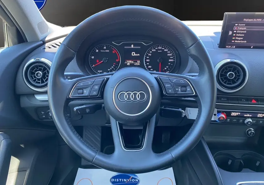 Vue centrée sur le volant cuir noir d'une Audi A3 Sportback 2020 avec tableau de bord et écran MMI en arrière-plan.