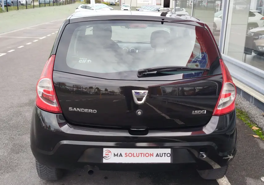 Vue arrière d'une Dacia Sandero noire de 2011, avec logo et badges visibles sur un parking extérieur.