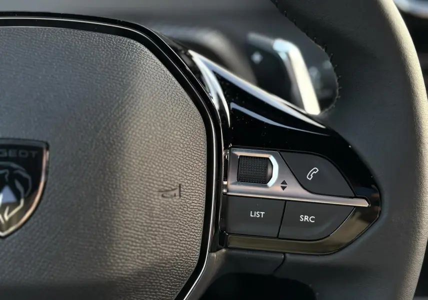 Gros plan sur le volant cuir noir du Peugeot 2008 Hybrid 145, avec commandes multimédia intégrées côté droit.
