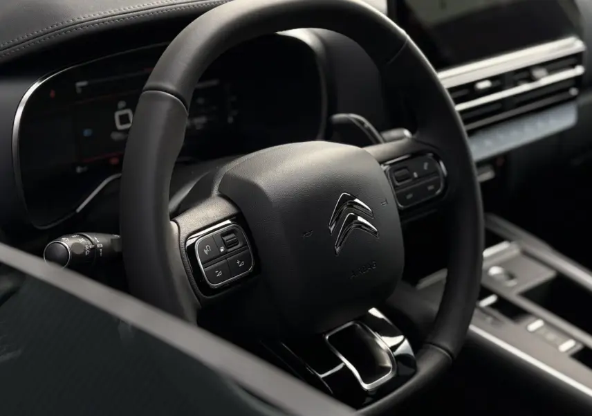 Vue rapprochée du volant noir en cuir du Citroën C5 Aircross 2025, avec commandes intégrées et tableau de bord numérique.