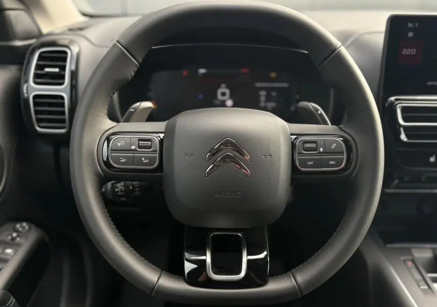 Vue centrée sur le volant cuir noir du Citroën C5 Aircross 2025 avec commandes intégrées et tableau de bord numérique flou.