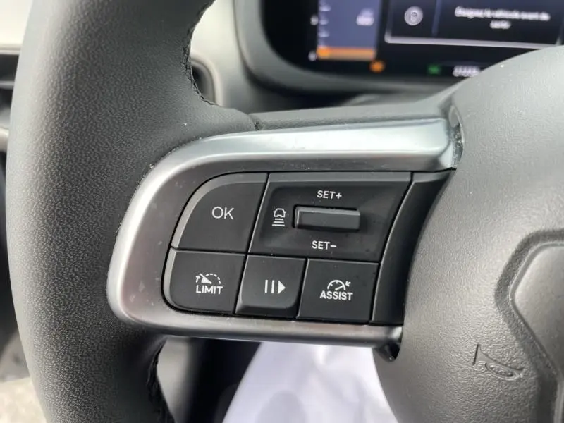 Gros plan sur les commandes au volant côté gauche du Jeep Avenger gris métal 2025, avec boutons de régulateur et assistance.