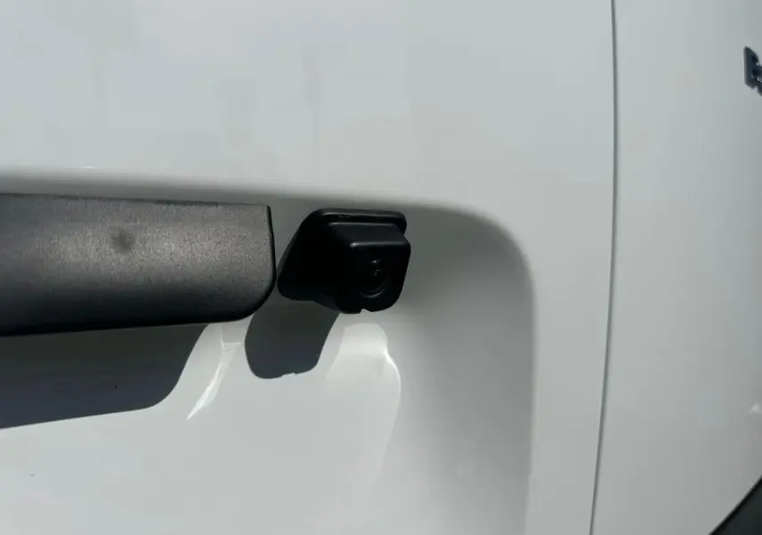 Gros plan sur la caméra de recul noire intégrée à la porte latérale blanche du Citroën Berlingo III Van.