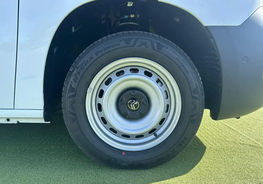 Gros plan sur la roue avant droite acier grise du Citroën Berlingo blanc Icy, avec pneu Nexen sur sol vert.