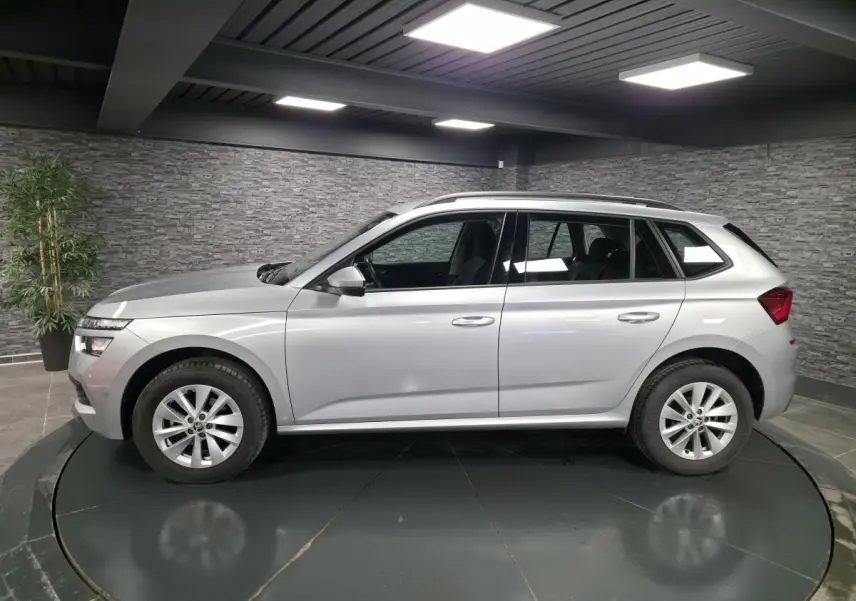 Vue latérale droite d’un Skoda Kamiq gris métallisé 2023, avec jantes alliage 16 pouces et barres de toit noires.