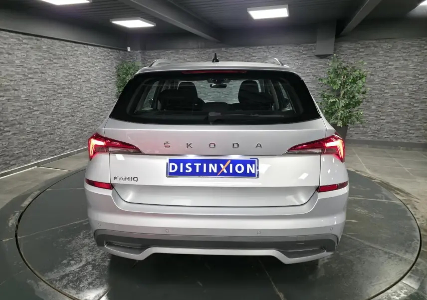 Vue arrière d'un Skoda Kamiq gris métallisé 2023 avec feux arrière LED et logo ŠKODA visible sur un plateau tournant intérieur.