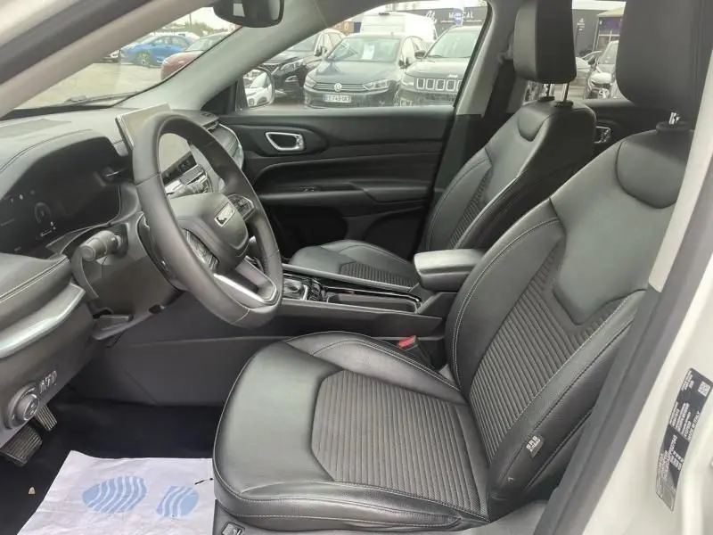 Vue intérieure côté conducteur du Jeep Compass blanc 2023, sièges cuir noirs et tableau de bord moderne avec écran digital.