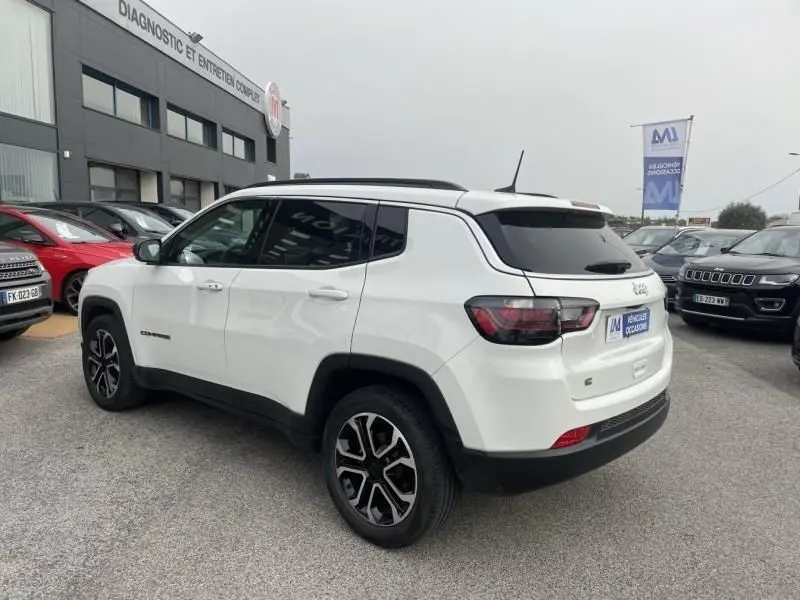 Jeep Compass blanc en vue 3/4 arrière côté gauche, avec jantes noires et toit panoramique noir visible.