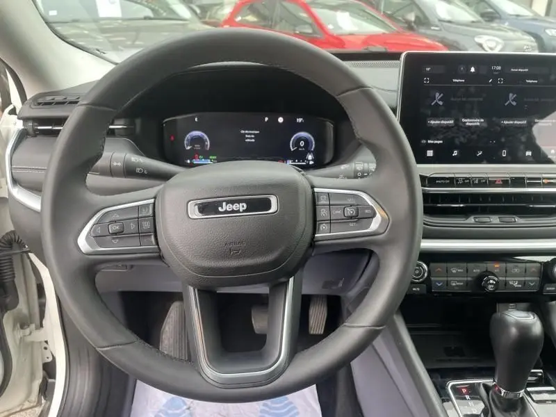 Vue intérieure centrée sur le volant noir du Jeep Compass blanc 2023, avec tableau de bord numérique et écran tactile visible.