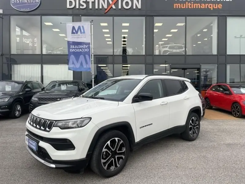 Jeep Compass blanc en 3/4 avant droit, avec jantes noires et détails noirs contrastants, devant un showroom multimarque.