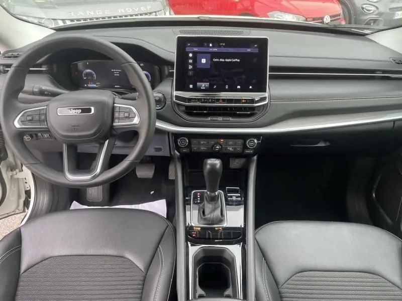 Vue intérieure avant du Jeep Compass 2023 blanc, avec tableau de bord moderne et écran tactile central.