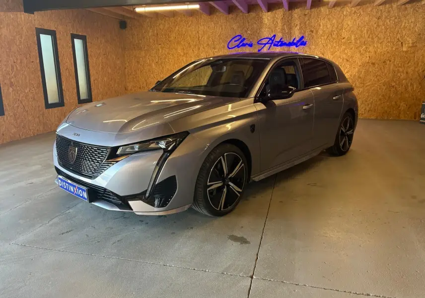 Peugeot 308 gris vue 3/4 avant droit en intérieur, avec calandre distinctive et jantes noires bicolores.