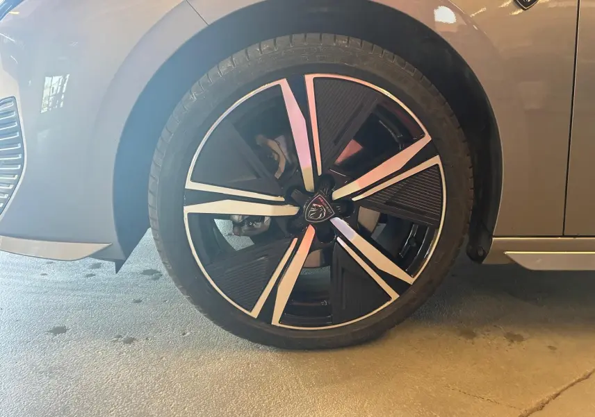 Gros plan sur la roue avant gauche d’une Peugeot 308 gris 2025, jante noire et argent avec logo lion au centre.