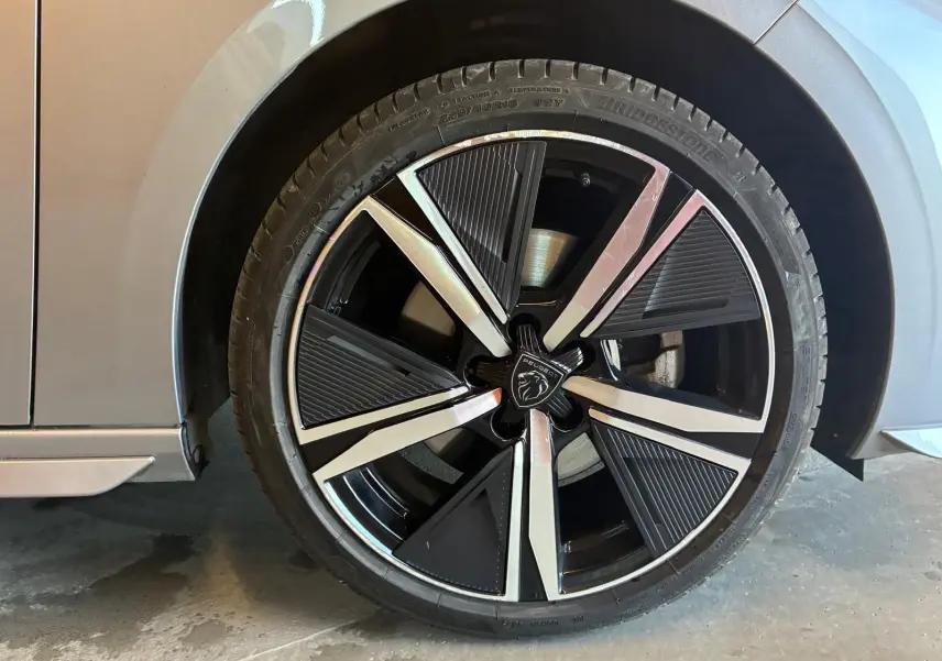Gros plan sur la roue avant droite grise d'une Peugeot 308 1.2 Hybrid 136 E-DCS6 GT avec jante noire et argentée.