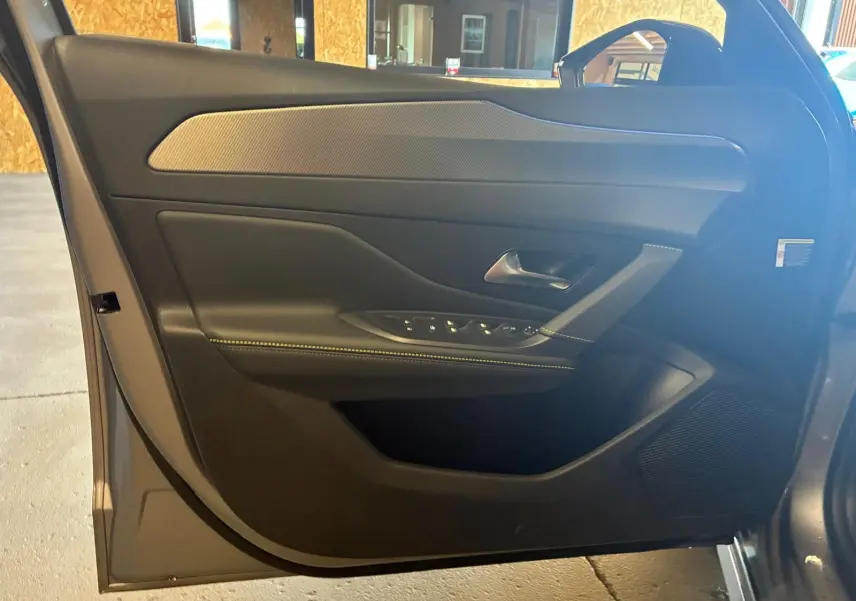 Vue rapprochée de la porte avant gauche gris métallisé de la Peugeot 308 1.2 Hybrid 136 E-DCS6 GT avec commandes de vitres et haut-parleur intégré.