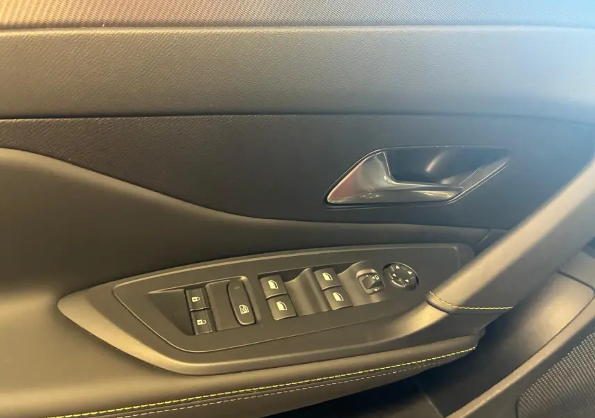Gros plan sur la porte côté gauche intérieure de la Peugeot 308 gris, avec commandes électriques et surpiqûres vertes.
