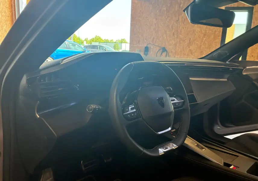 Vue intérieure côté conducteur de la Peugeot 308 gris 1.2 Hybrid 136 E-DCS6 GT avec volant multifonction et tableau de bord moderne.