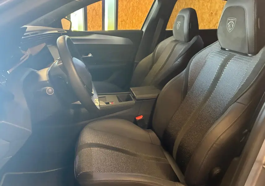 Vue intérieure côté conducteur de la Peugeot 308 gris 2025, sièges noirs avec logo Peugeot brodé sur les appuie-têtes.