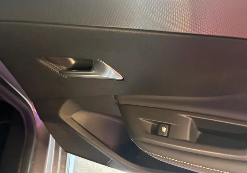 Détail de la porte intérieure côté gauche de la Peugeot 308 gris, avec poignée argentée et bouton de commande de vitre.