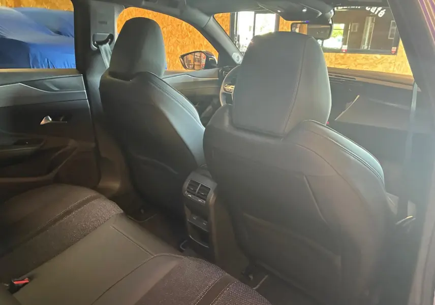 Vue intérieure arrière de la Peugeot 308 hybride 2025, sièges noirs et console centrale avec aérateurs visibles.