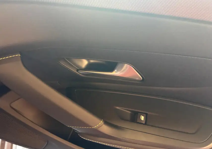Détail de la porte intérieure côté gauche de la Peugeot 308 gris, avec poignée argentée et couture jaune visible.