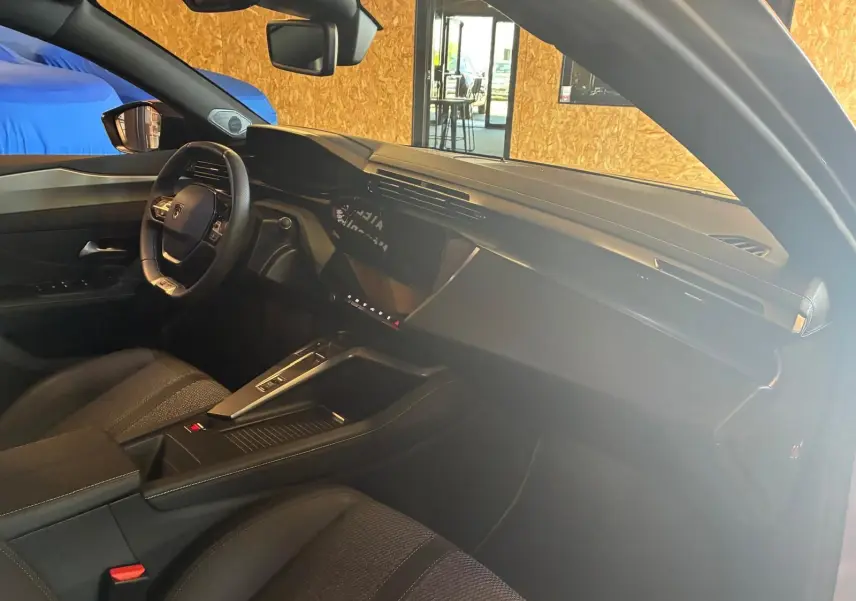 Vue intérieure côté conducteur de la Peugeot 308 gris 1.2 Hybrid 136 GT, avec tableau de bord moderne et volant compact.