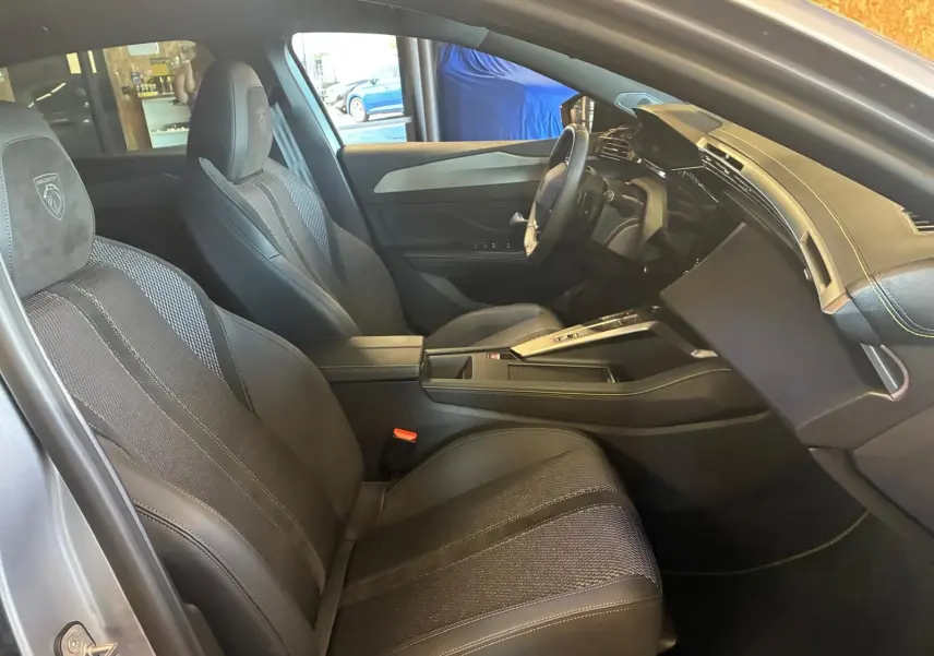 Vue intérieure côté conducteur de la Peugeot 308 gris 2025, sièges noirs avec surpiqûres et tableau de bord moderne.