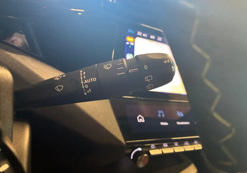 Gros plan sur la commande d’essuie-glace à gauche du volant dans l’habitacle sombre d’une Peugeot 308 gris 2025.