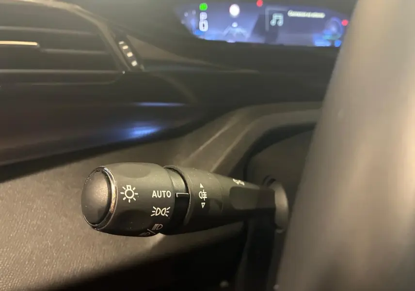 Gros plan sur la commande d’éclairage à gauche du volant dans l’habitacle noir de la Peugeot 308 gris 1.2 Hybrid 136 E-DCS6 GT 2025.