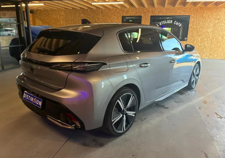 Vue 3/4 arrière droite d'une Peugeot 308 gris métallisé avec jantes alliage et feux arrière LED, stationnée en intérieur.