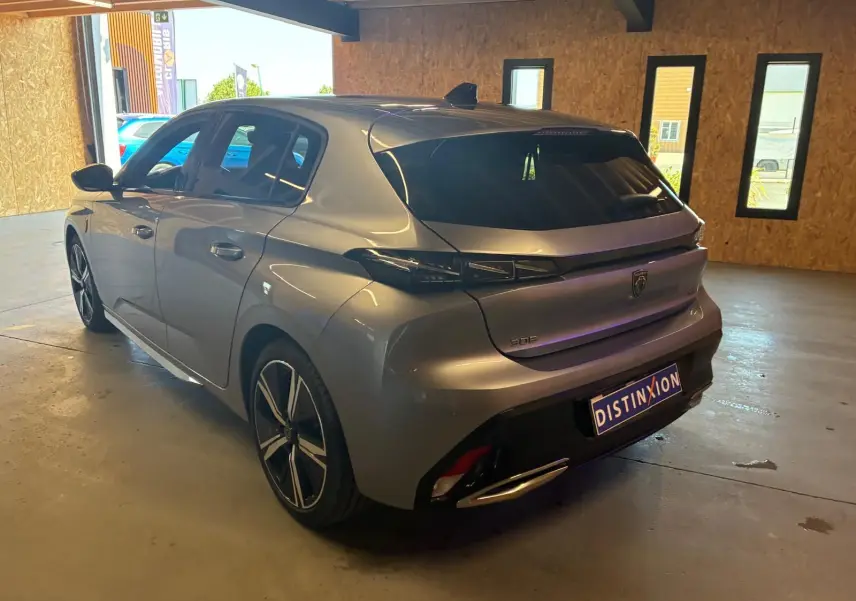 Vue 3/4 arrière droite d'une Peugeot 308 gris métallisé 2025 en hybride, avec feux arrière noirs et jantes sport.