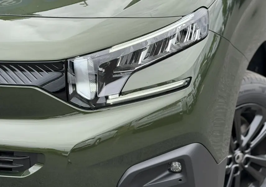Gros plan sur le phare avant droit et la calandre du Citroën Berlingo Multispace M vert Sirkka avec jante alliage noire.