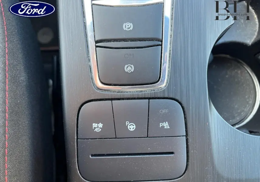 Vue rapprochée du panneau de commandes central noir et argenté avec boutons d’aide à la conduite dans un Ford Kuga noir.