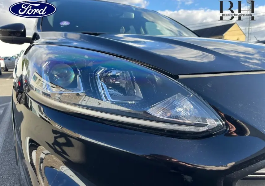 Gros plan sur le phare avant gauche du Ford Kuga noir Agate Métallisée, mettant en valeur son design moderne et précis.