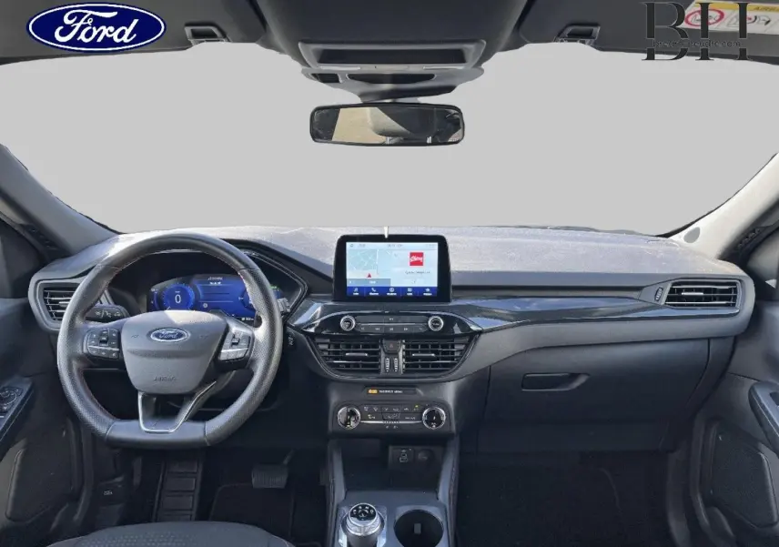 Vue frontale de l'intérieur du Ford Kuga 2023, tableau de bord noir avec écran tactile central et volant multifonction cuir.
