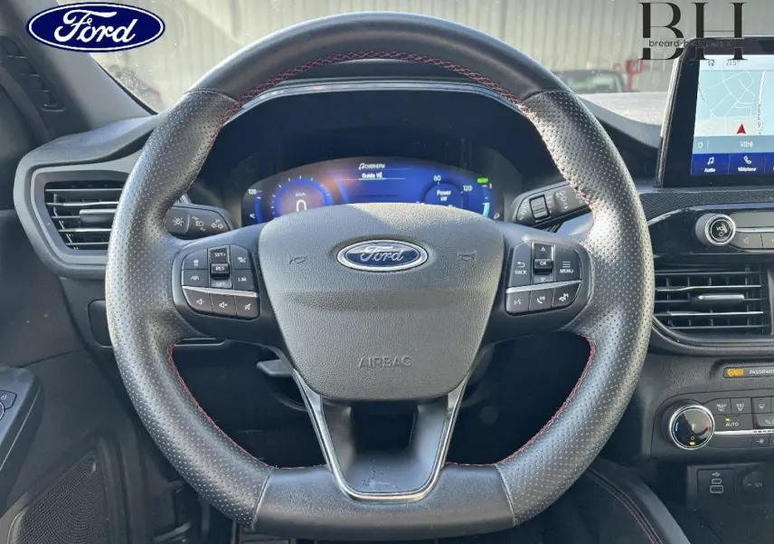 Vue frontale du volant cuir perforé noir avec surpiqûres rouges du Ford Kuga 2023, tableau de bord numérique et écran tactile GPS visible.