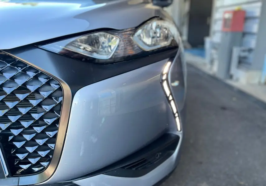 Gros plan sur l'avant droit gris métallisé du DS3 Crossback Performance Line, mettant en valeur la calandre et les feux LED.