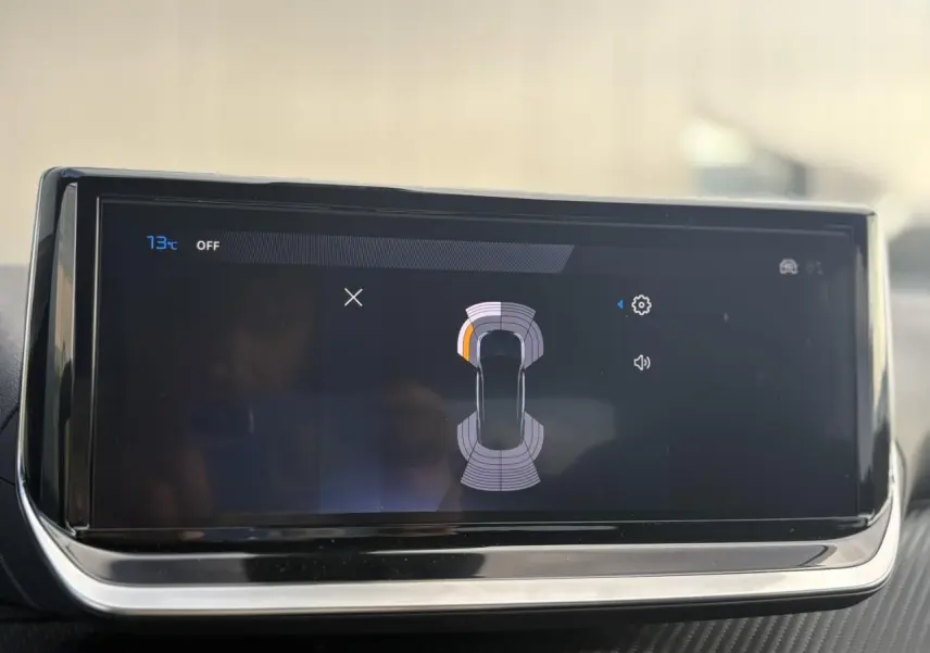 Écran tactile du tableau de bord du Peugeot 2008 Hybrid 145, affichant l'aide au stationnement avec vue du véhicule en plan.
