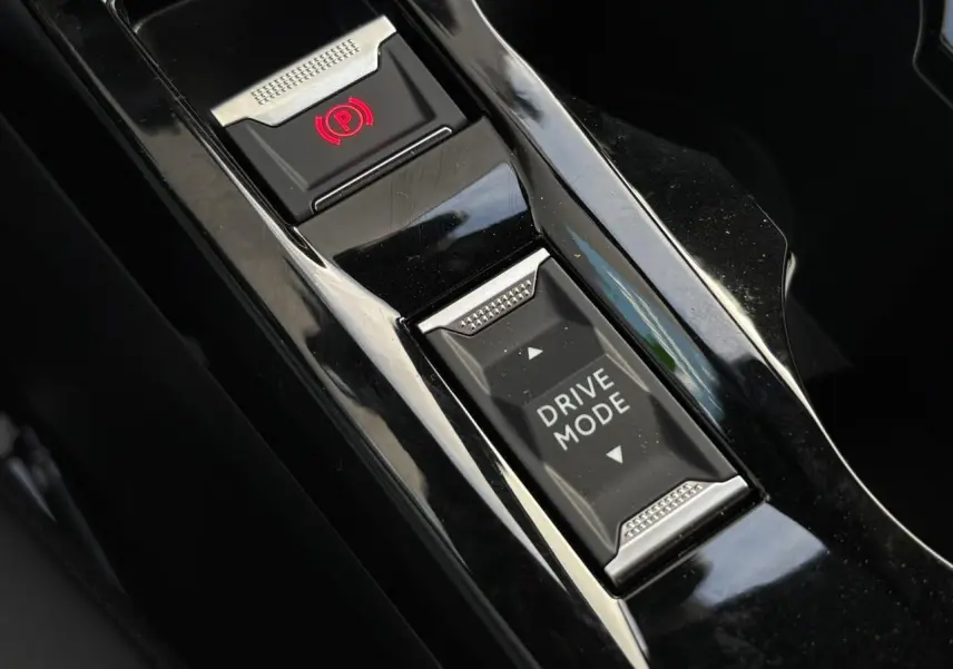 Gros plan sur la console centrale noire brillante du Peugeot 2008 Hybrid avec bouton Drive Mode et frein de stationnement électrique.