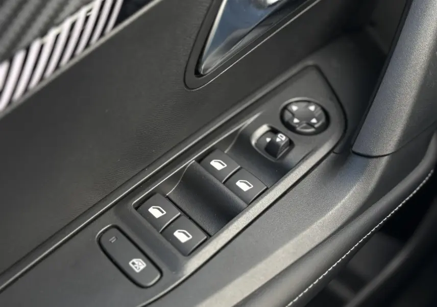 Gros plan sur les commandes de lève-vitres électriques côté conducteur, finition noire avec surpiqûres blanches.