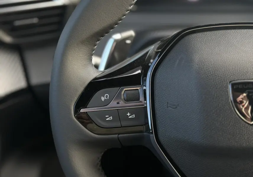 Gros plan sur le volant cuir noir du Peugeot 2008 Hybrid 145 e-DSC6 Allure avec commandes multimédia intégrées.