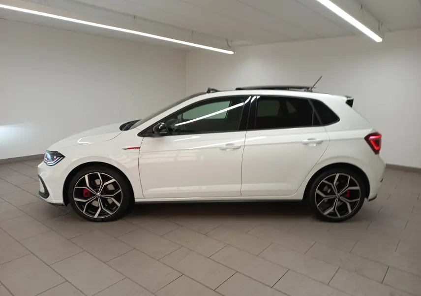 Vue de profil côté gauche d'une Volkswagen Polo GTI 2024 blanc pur avec toit noir et jantes sport noires et rouges.