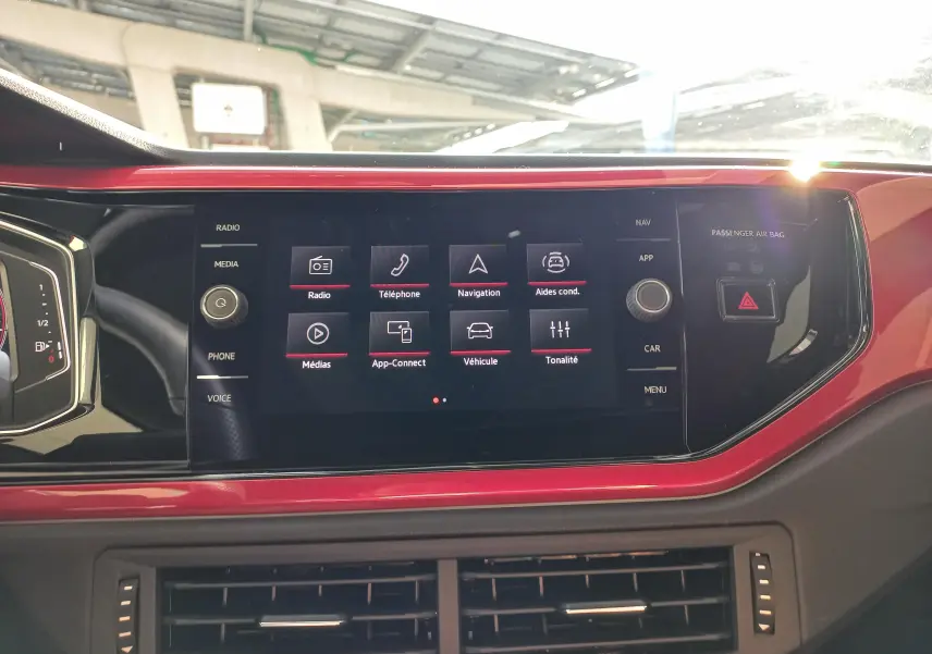Vue rapprochée de l'écran tactile central rouge et noir du tableau de bord de la Volkswagen Polo 2024 GTI avec interface multimédia affichée.