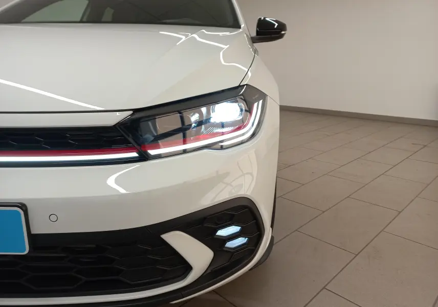 Gros plan sur l'avant droit de la Volkswagen Polo GTI 2024 blanc pur avec toit noir, phare allumé et détails rouges sur la calandre.